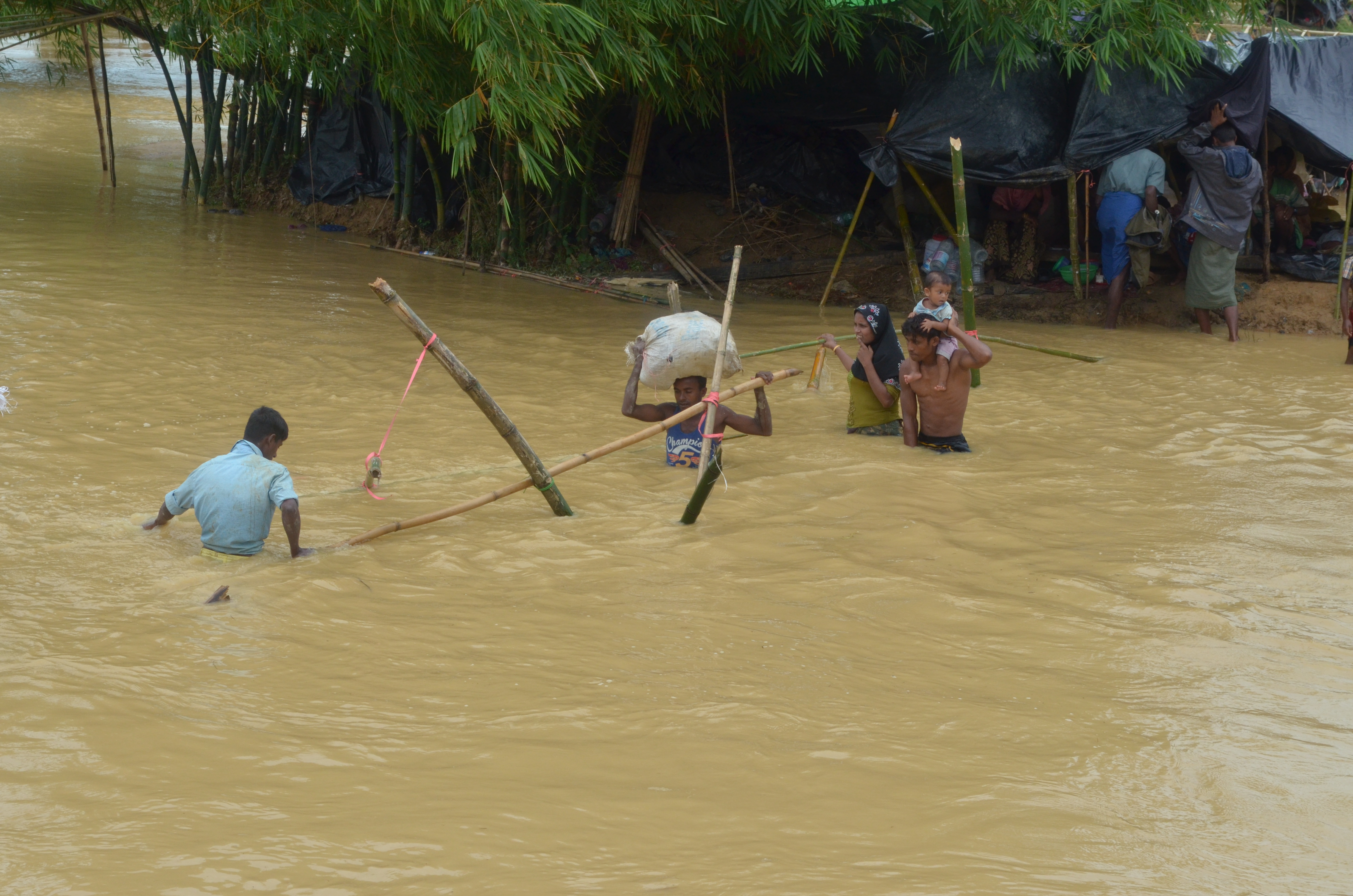 Rohingya refugees attempting to swim to the main road away from their tents which are surrounded by dirty flood water
